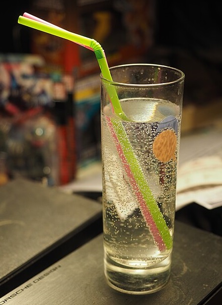 Glass of gin and tonic with multicoloure sraw leaning lef