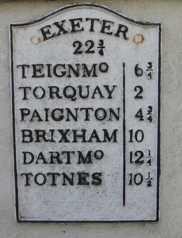 White metal mile-plate with names and mileages in black