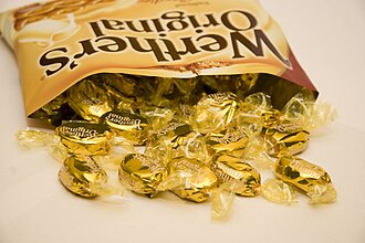 Open bag of Wether's Oiginals. Some sweets in front of bag. Black lettering on yellow